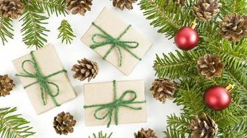 postal navideña con cajas de regalo artesanales, ramas de abeto, conos y adornos navideños rojos sobre un fondo blanco.
