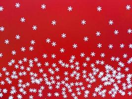 Scattered white snowflakes on red background. Simple festive flat lay. Stock photo. photo