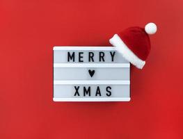 Feliz Navidad saludo en caja de luz con gorro de Papá Noel sobre un fondo rojo.