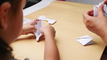 primo piano di madre e figlia che imparano l'arte giapponese di piegare la carta in forme e figure decorative a casa. video