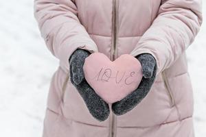 Women's hands in warm gray mittens with a snowy pink heart. The Concept Of Valentine's Day. The inscription on the heart Love photo