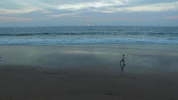 photo aérienne d'un petit garçon jouant au football sur la plage au coucher du soleil.