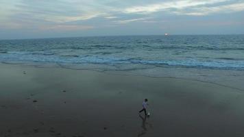 photo aérienne d'un petit garçon jouant au football sur la plage au coucher du soleil.