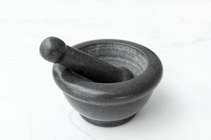 Black stone mortar and pestle isolated on white marble table photo