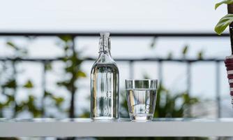 Beber una botella de agua con vidrio sobre la mesa en el jardín de la casa foto
