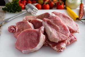 Raw meat, pork steaks on kitchen  table. Vegetables and meat hammer in the background. photo