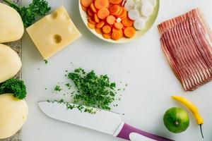 Sliced parsley with knife, potato, cheese, bacon, some onion and herbs on table. photo