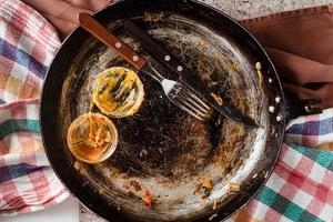 platos sucios vacíos, final de una deliciosa comida, sartén rústico, tenedor y cuchillo, y un tazón vacío de mostaza y salsa de tomate. foto