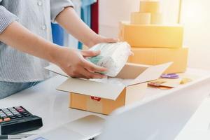 Closeup view of female's online store, small business owner seller, entrepreneur packing package, post shipping box preparing delivery parcel on the table, entrepreneurial self-employed business concept