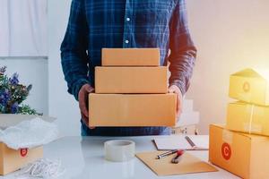 Vista cercana de la tienda en línea del hombre, vendedor propietario de una pequeña empresa, emprendedor paquete de embalaje caja de envío postal preparando el paquete de entrega sobre la mesa, concepto de negocio emprendedor autónomo foto