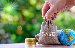 Hand holding a money bag with coins and a globe on a bokeh nature background photo