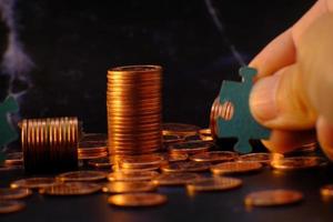 A person holding a puzzle piece next to a stack of coins photo