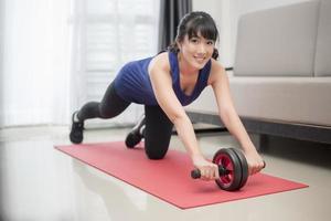 Beautiful sporty woman  do abdominal exercises with wheel at home photo