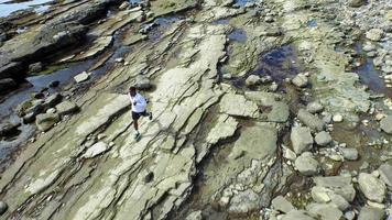 tracking shot van een jonge man die loopt op een rotsachtige kustlijn van het oceaanstrand. video