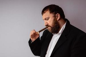 Bearded man in modern coat and shirt lighting his cigar photo