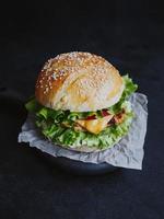 apetitosa hamburguesa casera fresca, con chuleta de pollo, lechuga, tomate, queso y salsa. sobre una tabla de madera sobre un fondo negro foto