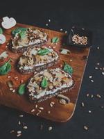 Sabrosa bruschetta fresca con champiñones, espinacas, ajo, queso crema y piñones, sobre una tabla de madera, sobre un fondo oscuro. foto