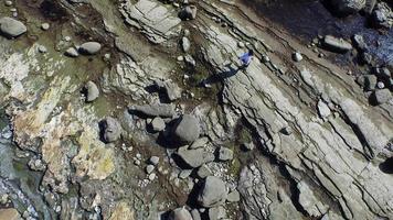 Aerial shot of young man running on a scenic rocky beach coastline. video