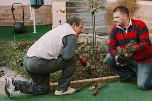 Joven adulto maduro ayudando a hombres mayores con trabajos de jardinería foto