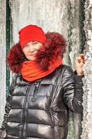 Portrait of a woman in a red hat and scarf, warm jacket against the background of an ice wall. Winter photo