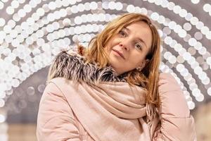 A pretty young woman stands in a shopping center with a bokeh of many light bulbs in the background. photo