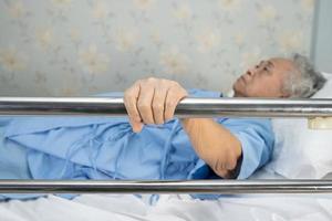 Paciente asiático mayor o anciana acostarse, manejar la cama de riel con esperanza en una cama en el hospital foto