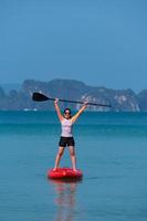 Joven mujer deportiva jugando stand-up paddle board en el mar azul en un día soleado de vacaciones de verano