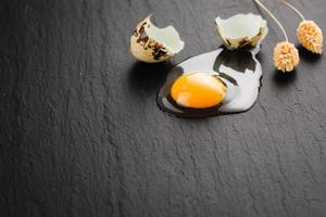 Quail eggs on black stone background, broken, cracked quail egg, yolk of quail egg. Organic product. photo