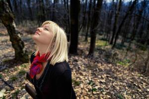 mujer rubia con pañuelo rojo y camisa negra en el bosque mirando hacia el cielo. primavera, retrato al aire libre. foto