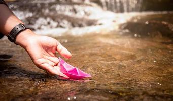Close up of Woman's hand putting paper boat on the water and pushing it away with reflection sunshine in the water background, as in childhood. photo