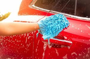 Cerca de la mano está lavando el coche por guante con jabón de burbujas al aire libre.