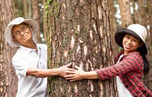 An adult daughter with senior father hugging a tree in the woods. Earth's day concept with people protecting the trees from deforestation. photo