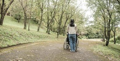 parte trasera del abuelo feliz en silla de ruedas relajándose y caminando con su nieta al aire libre en el parque. estilo de vida familiar feliz.