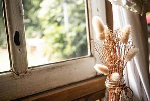 Dried flowers in a glass bottle on wooden table by the window with the sunshine coming in the room. Living room decoration. photo