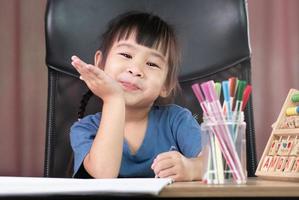 una linda niña dibuja un arco iris en papel con lápices de colores en la mesa de su casa. foto