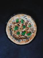 Homemade pizza with mushrooms, spinach, garlic, cream cheese and pine nuts, on a dark background. photo