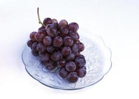 Frutos de uva roja en plato de vidrio aislado sobre fondo blanco. foto