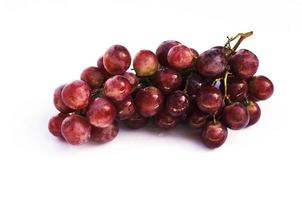 Frutos de uva roja en plato de vidrio aislado sobre fondo blanco.