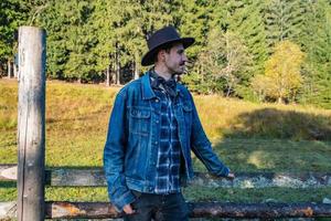 Cowboy in a denim jacket and hat near the fence in the mountains photo