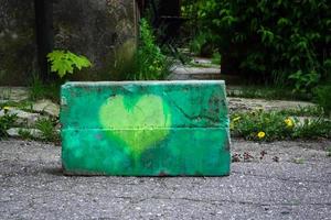 Corazón pintado de amarillo sobre hormigón con hierba diente de león y árboles en el fondo foto