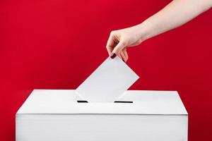 Woman puts a ballot paper in voting box on red background. Elections in the United States. photo