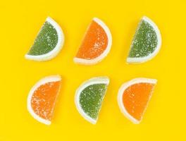 Rodajas de cítricos de mermelada de naranja y verde en azúcar sobre fondo amarillo.