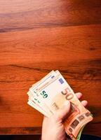 Hand holds stack of fifty euro banknotes wooden table background. Wages and minimum salary in europe union. photo