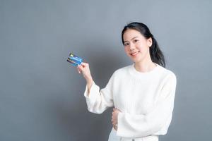 Retrato de una hermosa joven asiática en suéter mostrando tarjeta de crédito con espacio de copia foto
