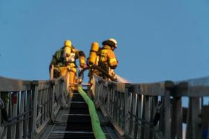 Bomberos subiendo la escalera contra el edificio y extinguiendo un incendio foto