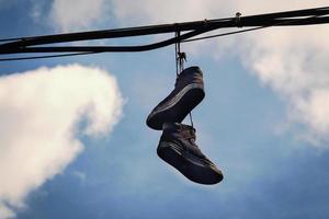 Two dirty old sneakers hanging on wires in blue sky with clouds photo