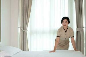 Hermosa joven sirvienta asiática arreglando una manta en la cama en la habitación del hotel foto