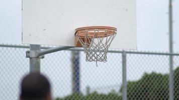 un joven tirando aros en una cancha de baloncesto al aire libre.