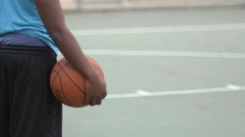 un giovane giocatore di basket in piedi su un campo da basket all'aperto in possesso di un pallone da basket. video