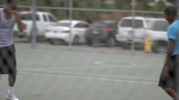 due giovani uomini che giocano insieme a basket uno contro uno su un campo all'aperto circondato da una recinzione di collegamento a catena. video